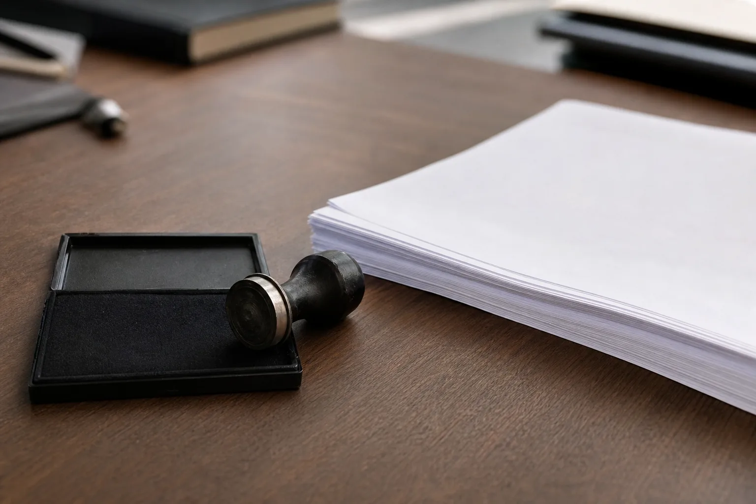 A notary stamp and an ink pad on a desk beside a stack of unmarked document pages